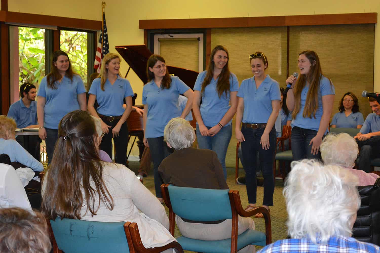 Six singers stand before a seated Broadview audience, one holding a microphone.