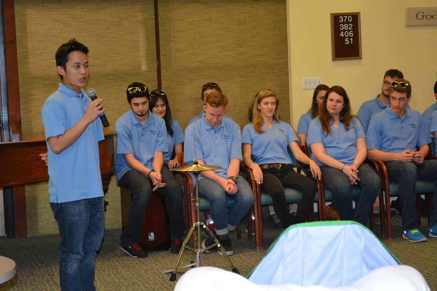 A performer speaks into a microphone while fellow Arts on Tour members sit behind.