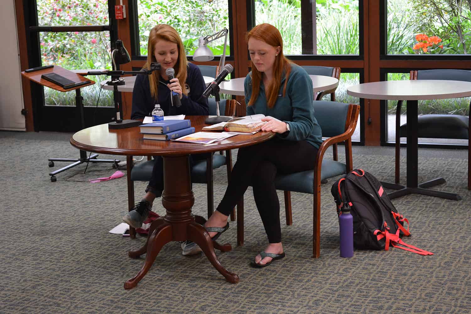 Two Principia tennis team members sit at a table with open books and microphones.