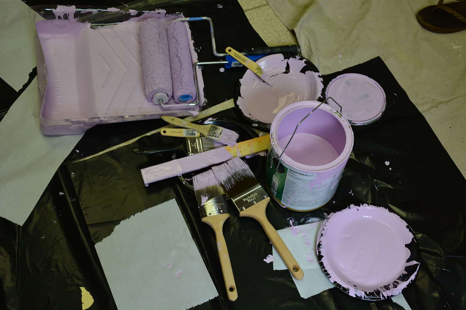 Paint rollers, brushes, trays, and buckets filled with lavender paint.