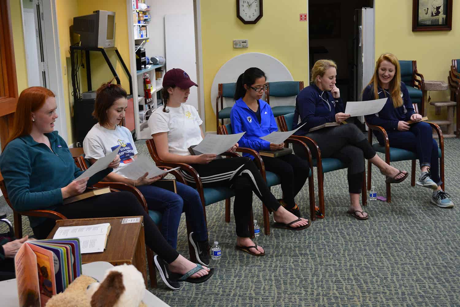 Six Principia tennis team members sit in a circle holding printed sheets.