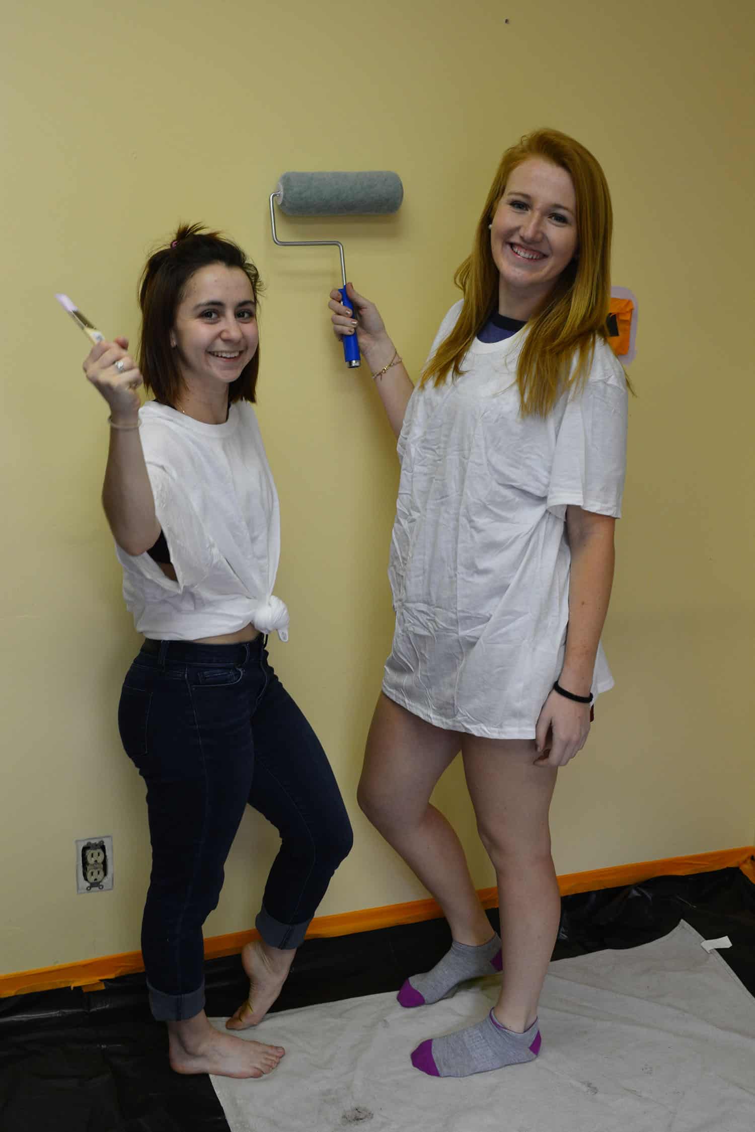 Two volunteers pose with a paintbrush and roller before painting the salon.