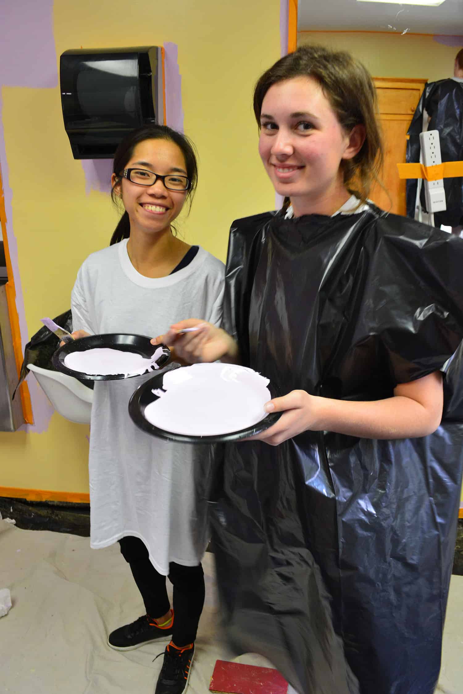 Two volunteers hold trays of lavender paint in the partly painted salon.