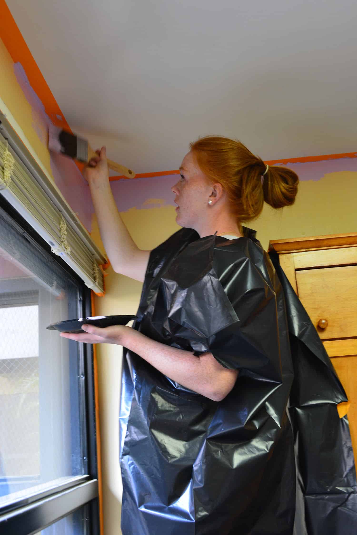 A volunteer paints lavender trim near the ceiling and window.