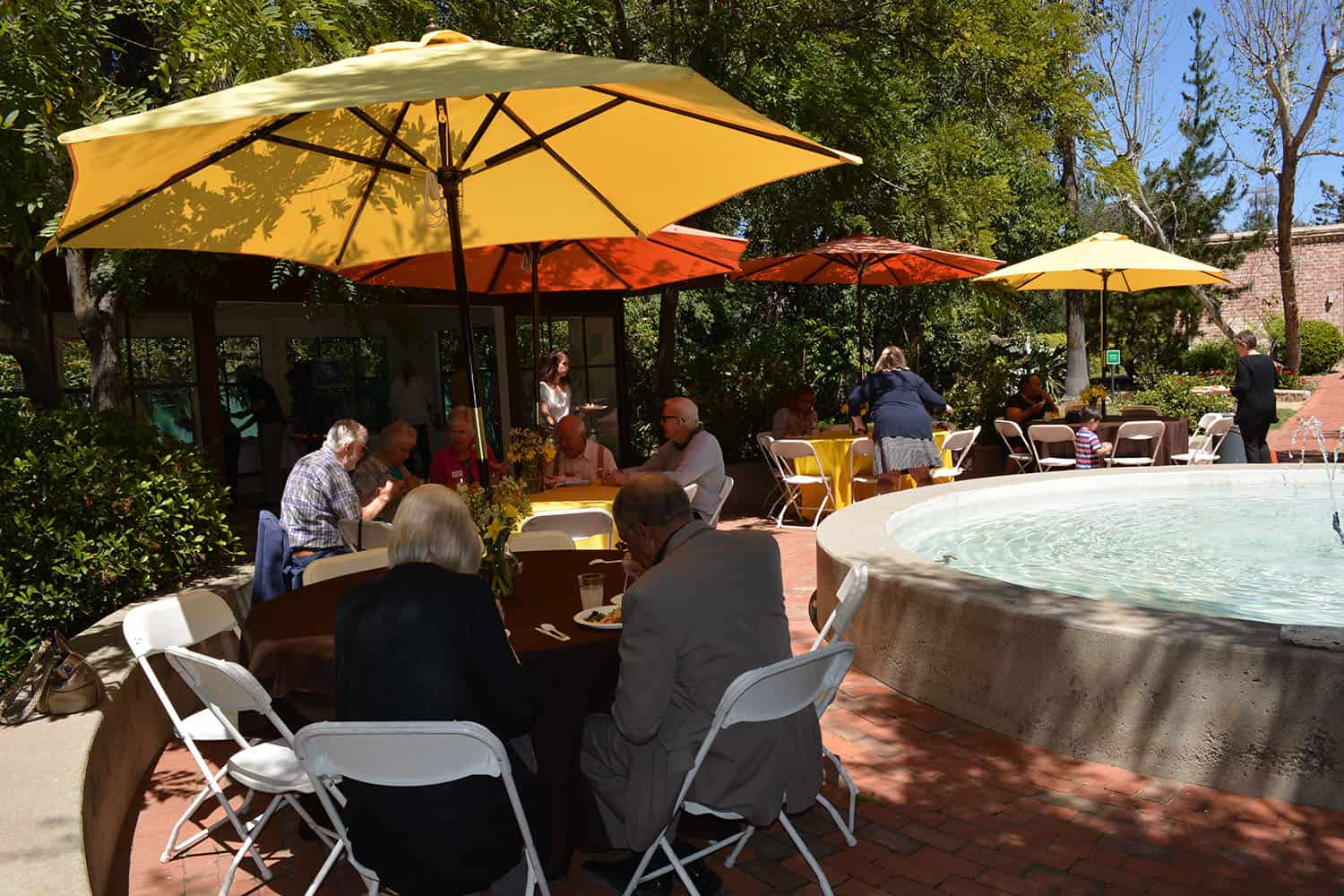 Workshop attendees eat lunch under colorful umbrellas beside the courtyard fountain.
