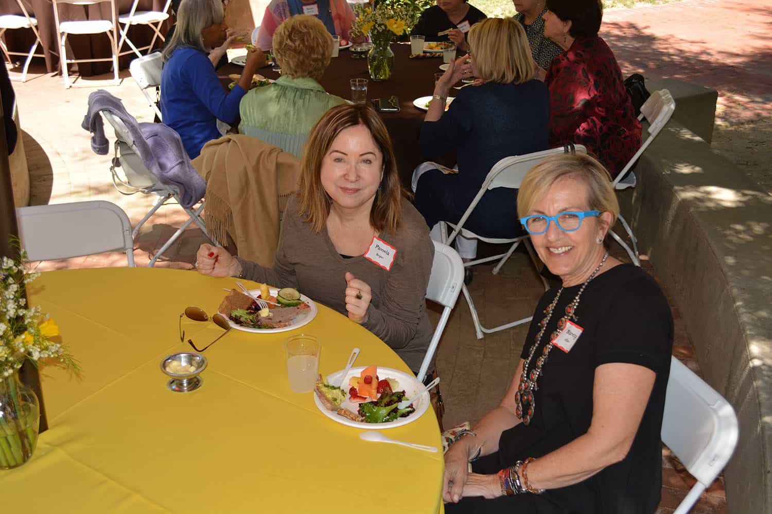 Two attendees smile over lunch at a yellow-covered courtyard table.