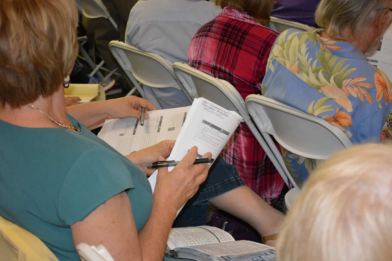 A workshop attendee takes notes with a handout and an open Bible on their lap.