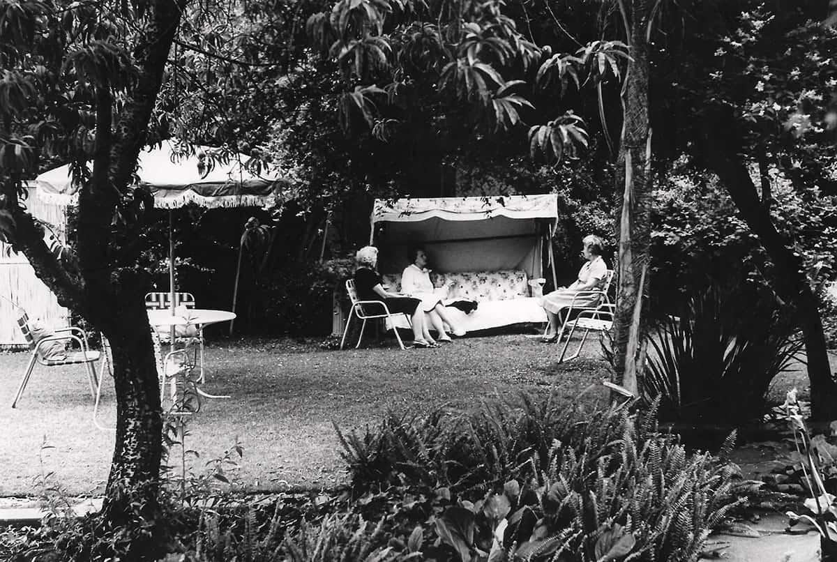 Three women sit together among canopy swings in a shaded garden.