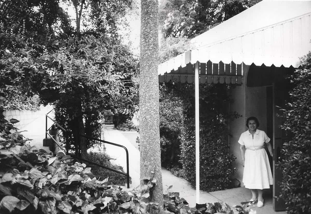 A woman in a white uniform stands at a covered entrance to Griffith Park Maternity Home.
